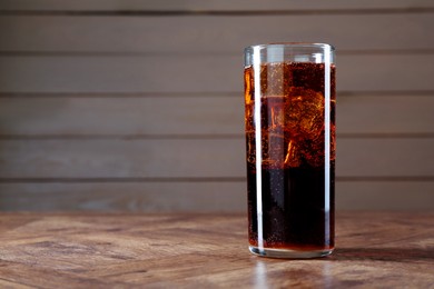 Photo of Sweet soda water with ice cubes in glass on wooden table, space for text