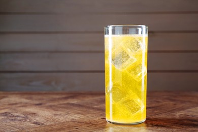 Photo of Sweet soda water with ice cubes in glass on wooden table, space for text