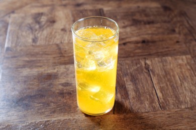 Photo of Sweet soda water with ice cubes in glass on wooden table