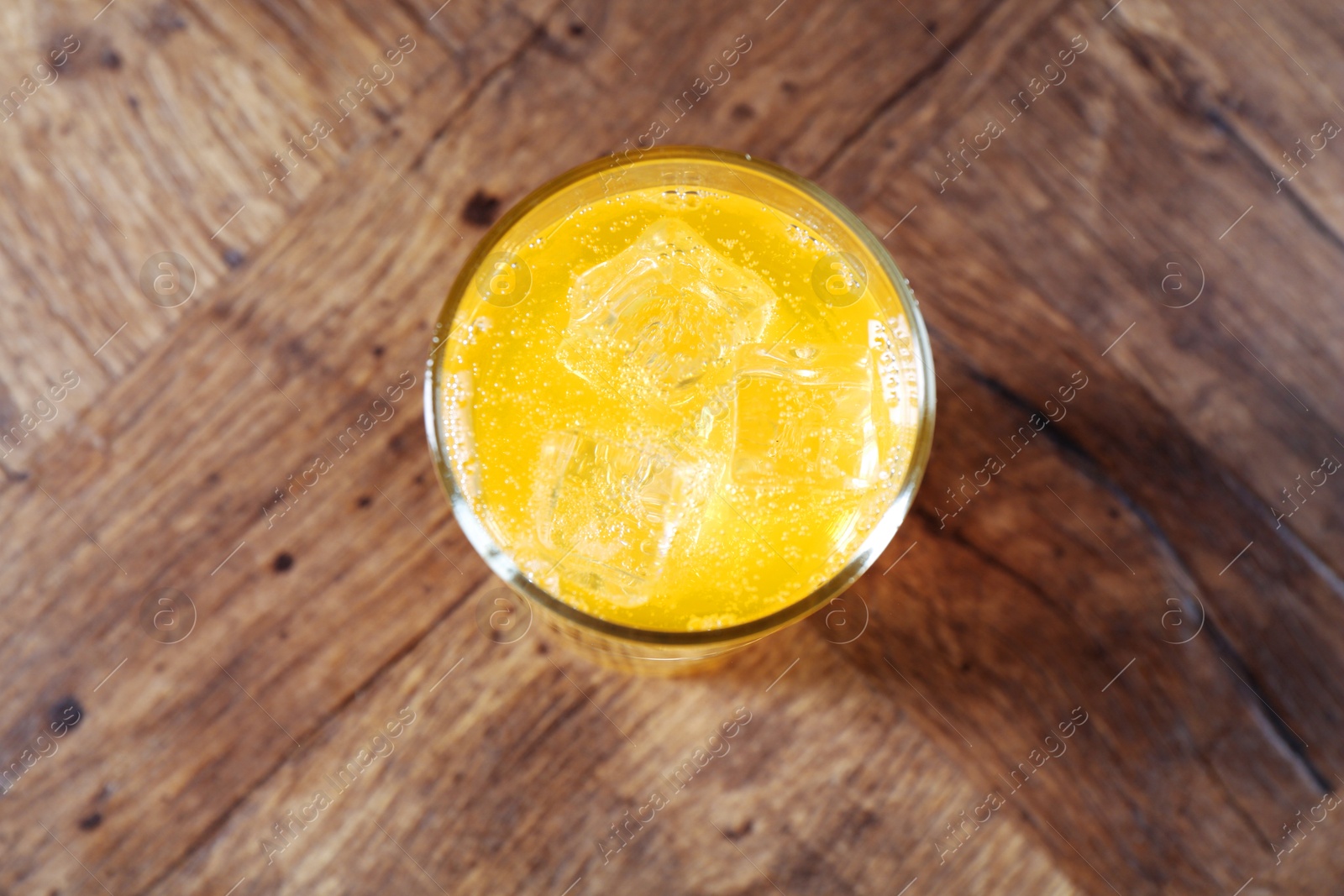 Photo of Sweet soda water with ice cubes in glass on wooden table, top view