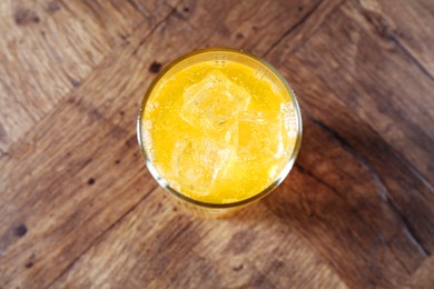 Photo of Sweet soda water with ice cubes in glass on wooden table, top view