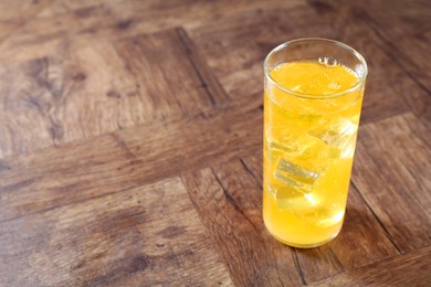 Photo of Sweet soda water with ice cubes in glass on wooden table. Space for text