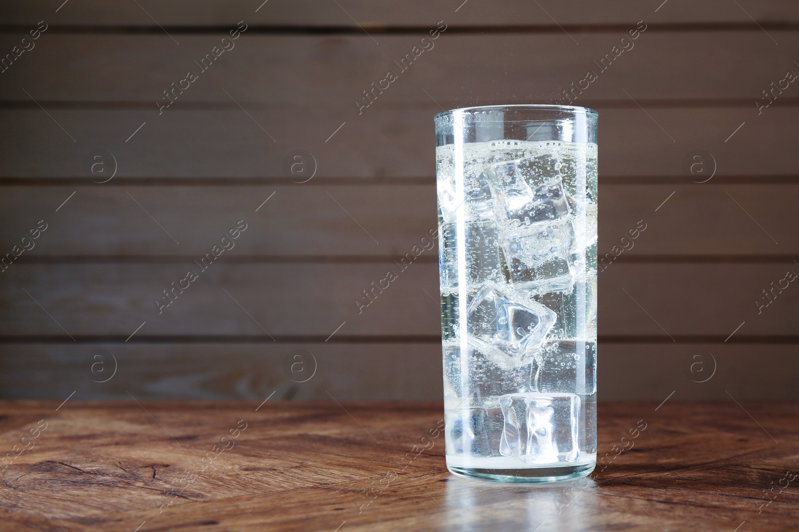 Photo of Refreshing soda water with ice cubes in glass on wooden table, space for text