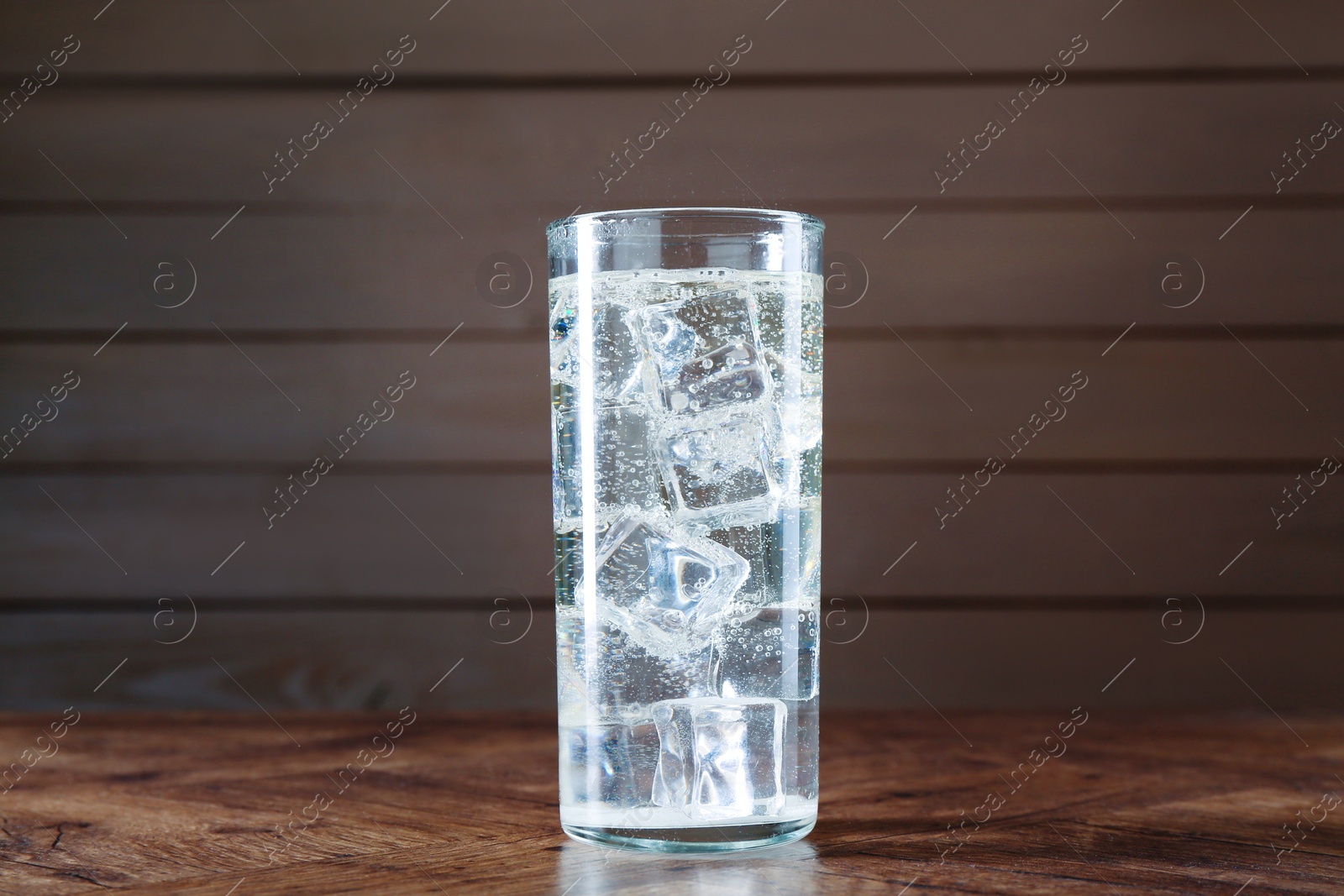 Photo of Refreshing soda water with ice cubes in glass on wooden table