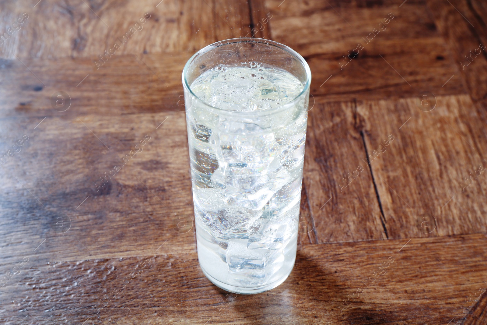 Photo of Refreshing soda water with ice cubes in glass on wooden table, closeup