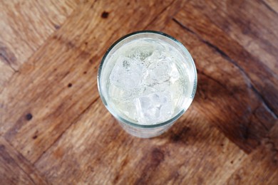 Photo of Refreshing soda water with ice cubes in glass on wooden table, top view