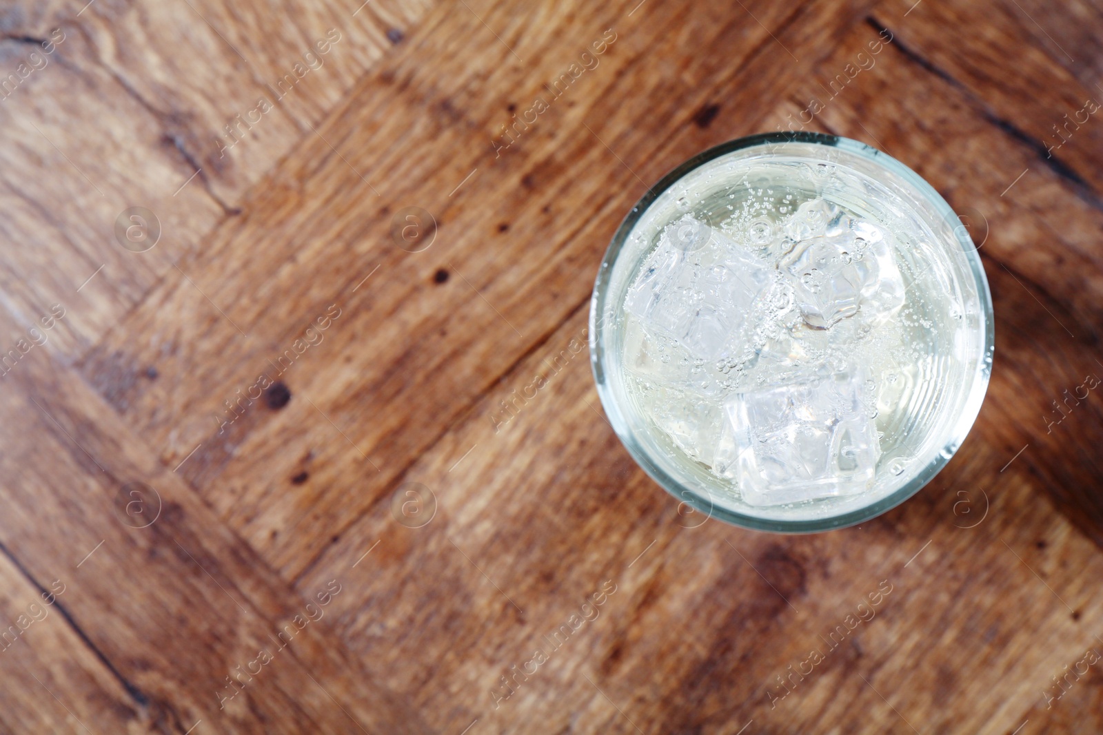 Photo of Refreshing soda water with ice cubes in glass on wooden table, top view. Space for text