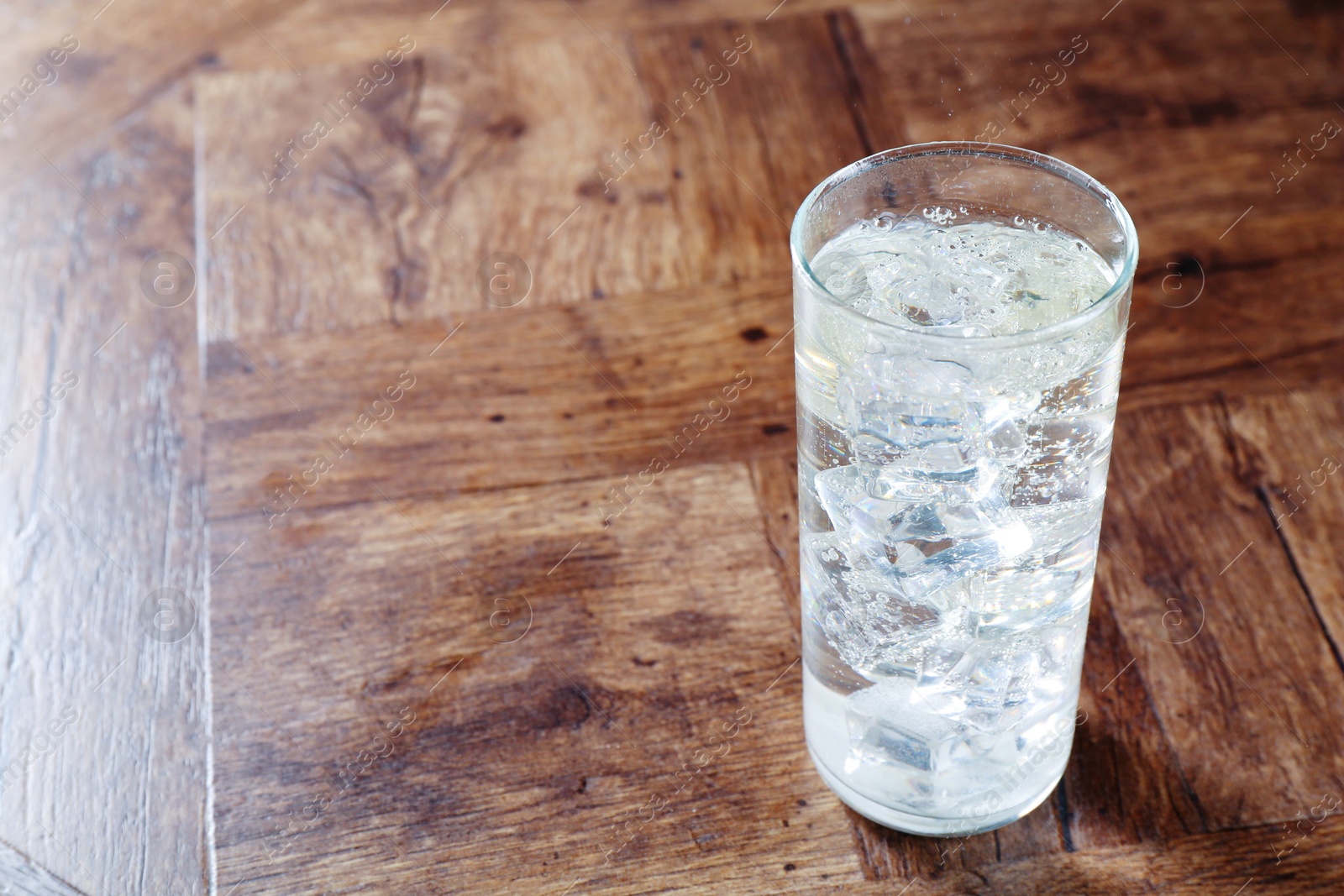 Photo of Refreshing soda water with ice cubes in glass on wooden table, space for text