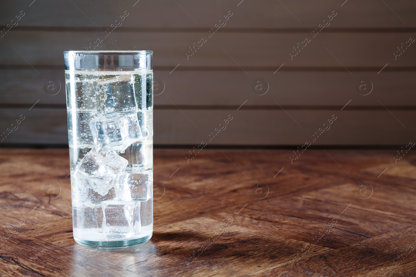 Photo of Refreshing soda water with ice cubes in glass on wooden table, space for text