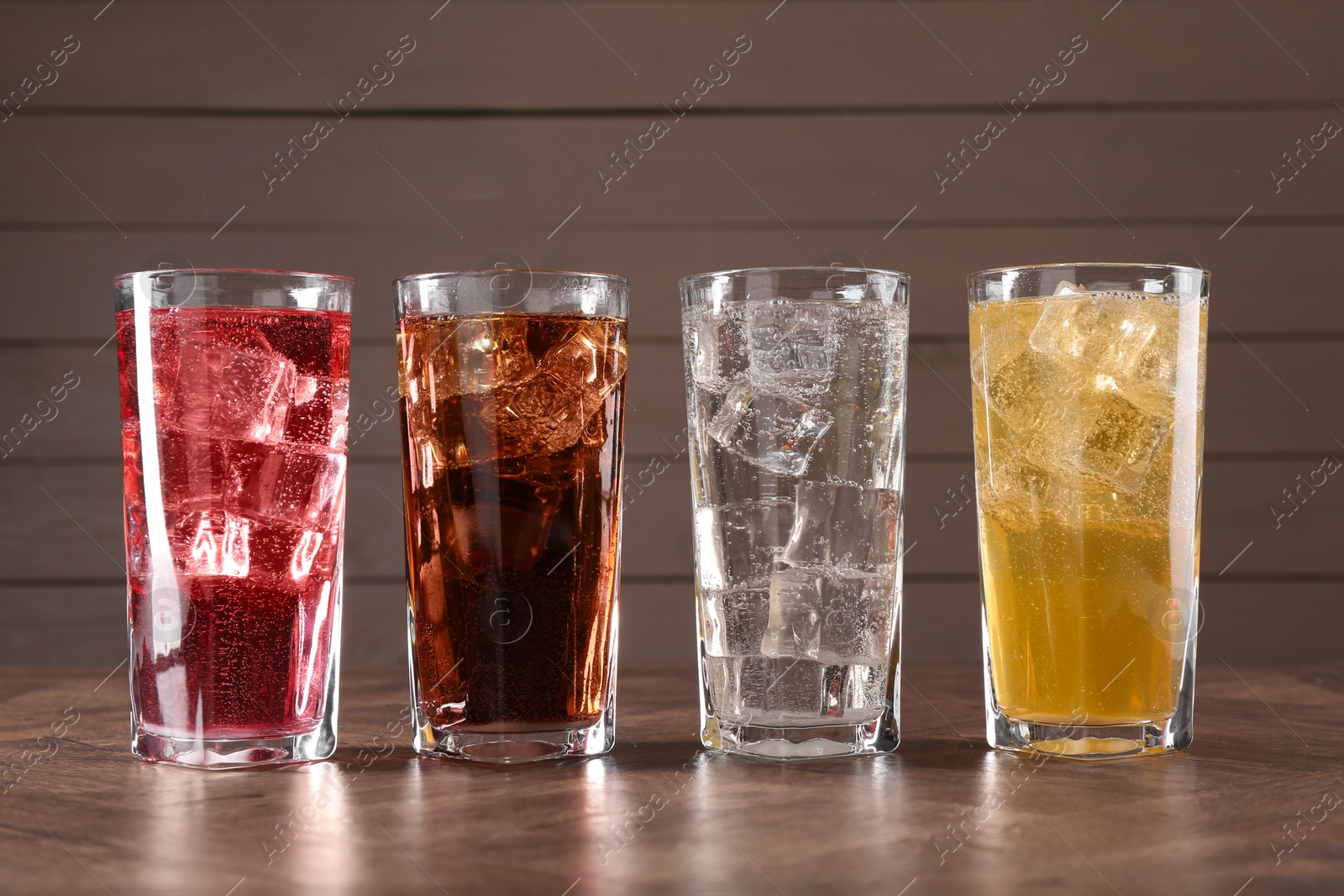 Photo of Refreshing soda water of different flavors with ice cubes in glasses on wooden table