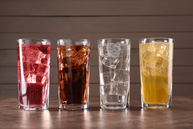 Photo of Refreshing soda water of different flavors with ice cubes in glasses on wooden table