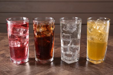 Photo of Refreshing soda water of different flavors with ice cubes in glasses on wooden table