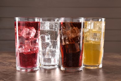 Photo of Refreshing soda water of different flavors with ice cubes in glasses on wooden table