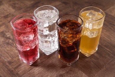 Photo of Refreshing soda water of different flavors with ice cubes in glasses on wooden table