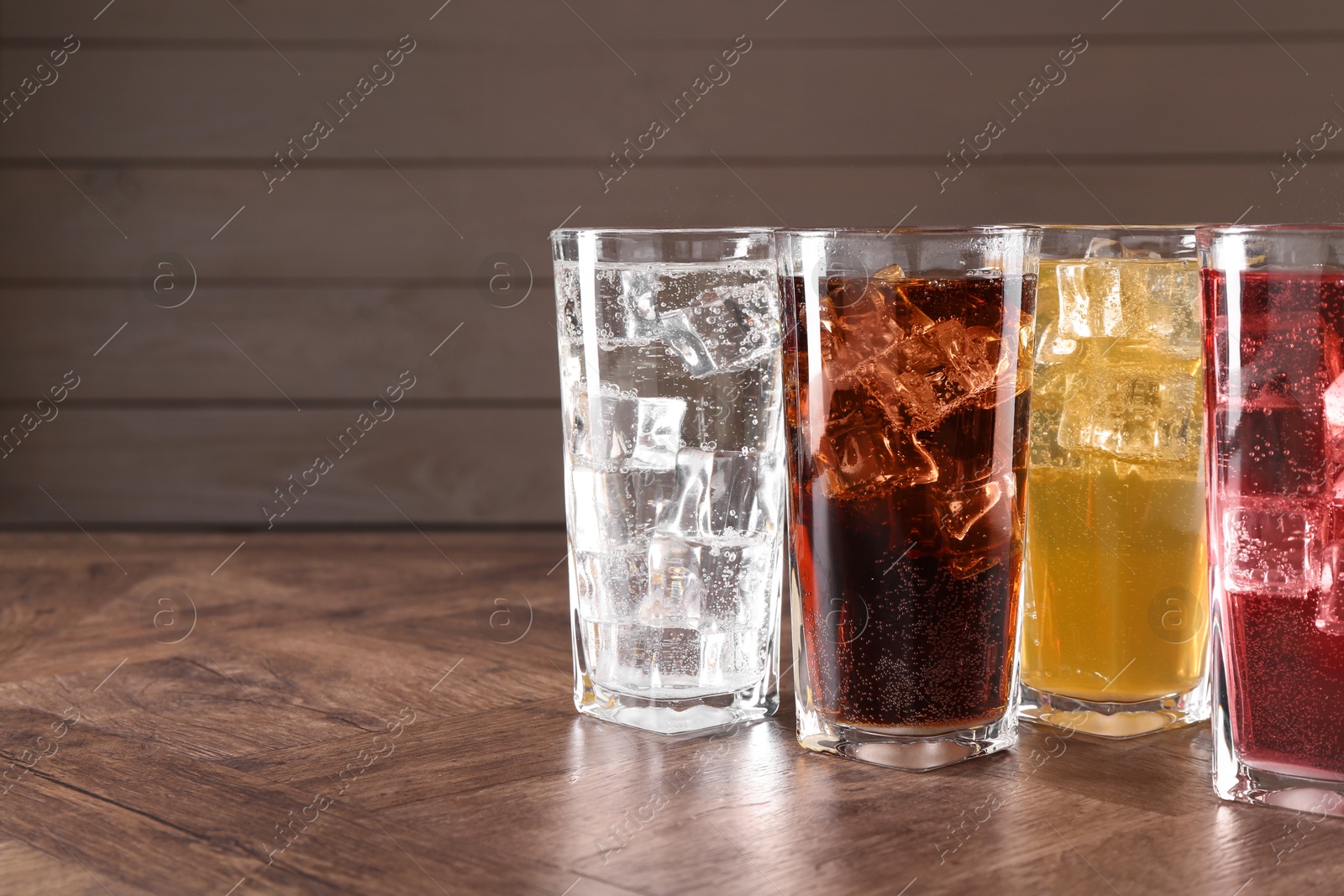 Photo of Refreshing soda water of different flavors with ice cubes in glasses on wooden table, space for text