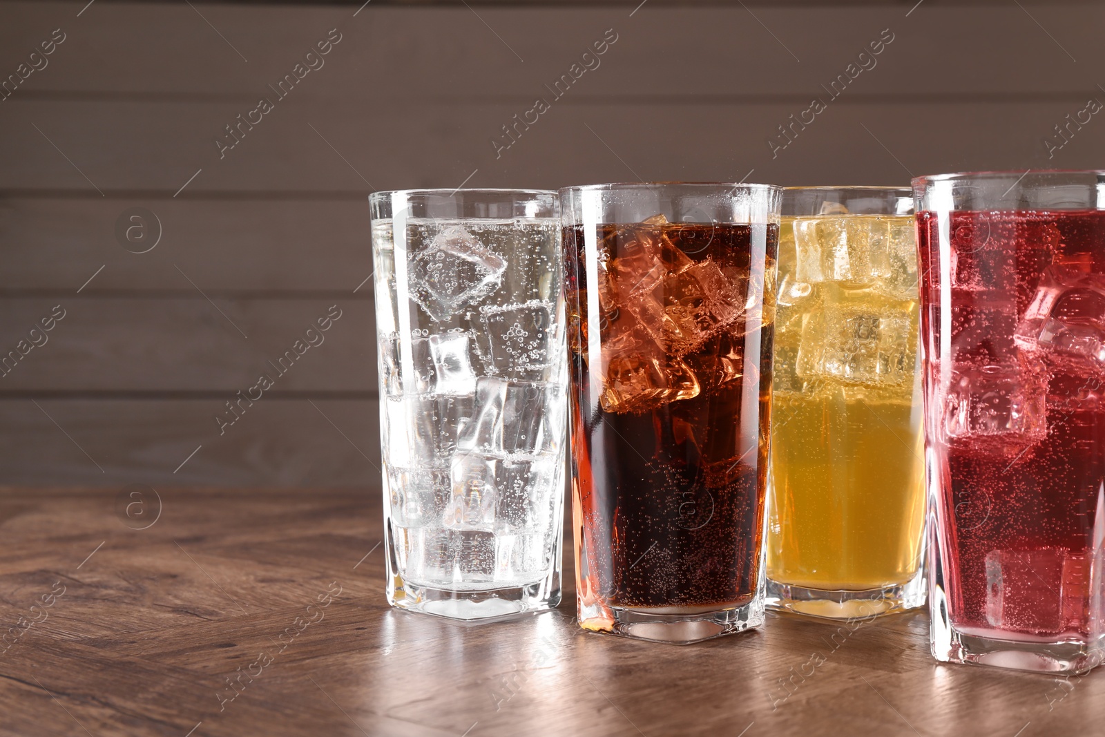 Photo of Refreshing soda water of different flavors with ice cubes in glasses on wooden table, space for text