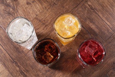 Photo of Refreshing soda water of different flavors with ice cubes in glasses on wooden table, flat lay