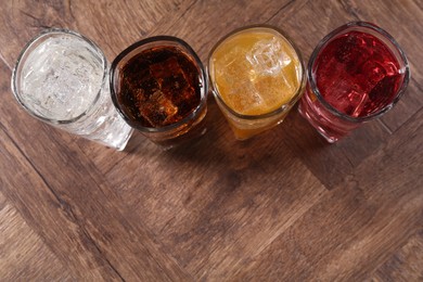 Photo of Refreshing soda water of different flavors with ice cubes in glasses on wooden table, flat lay. Space for text