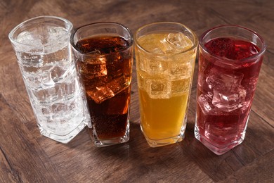 Photo of Refreshing soda water of different flavors with ice cubes in glasses on wooden table