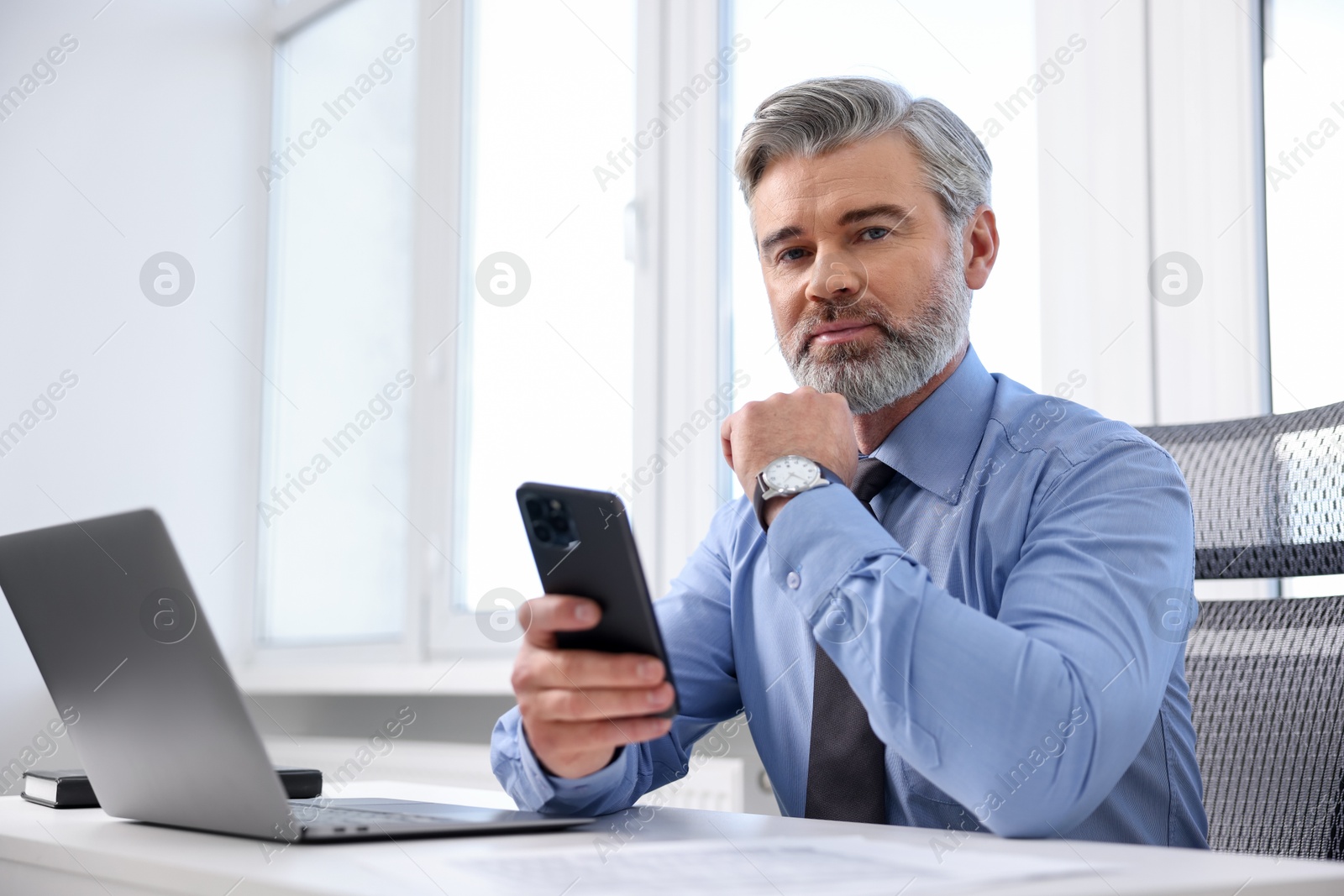 Photo of Banker with smartphone at desk in office