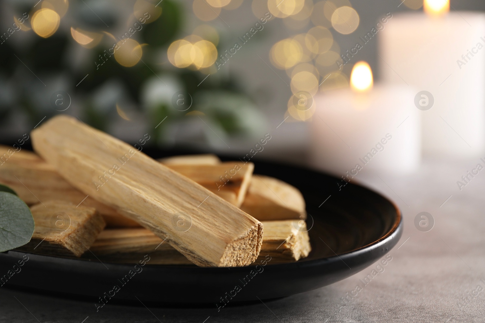 Photo of Palo santo sticks and burning candles on grey table, closeup