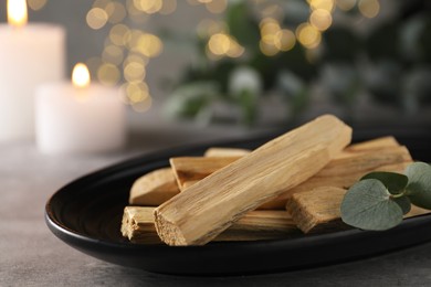 Photo of Palo santo sticks, eucalyptus branch and burning candles on grey table, closeup