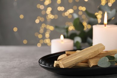 Photo of Palo santo sticks, eucalyptus branch and burning candles on grey table, closeup. Space for text