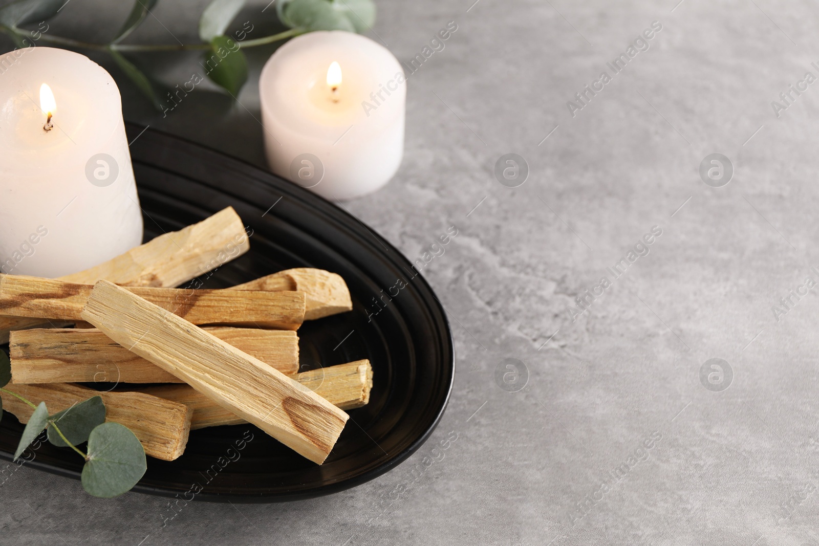 Photo of Palo santo sticks, eucalyptus branches and burning candles on grey table, closeup. Space for text