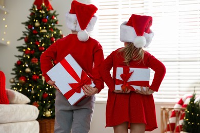 Photo of Little children in Santa hats with Christmas gifts at home, back view