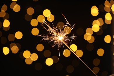 Photo of Bright burning sparkler on dark background with blurred lights, bokeh effect