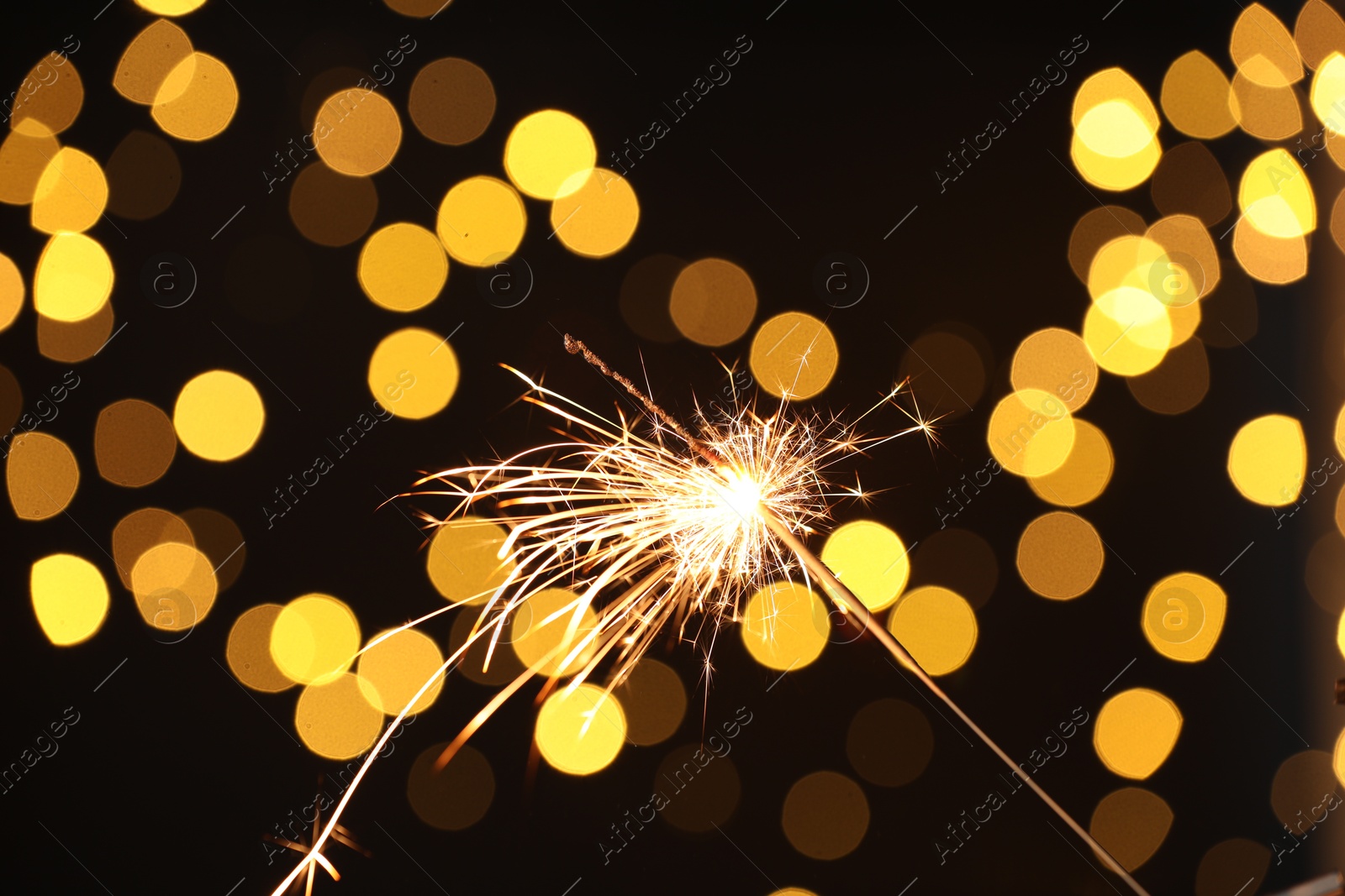 Photo of Bright burning sparkler on dark background with blurred lights, bokeh effect