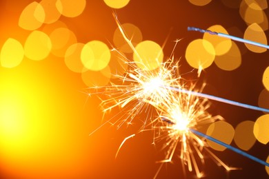 Photo of Bright burning sparklers on golden background with blurred lights, space for text. Bokeh effect