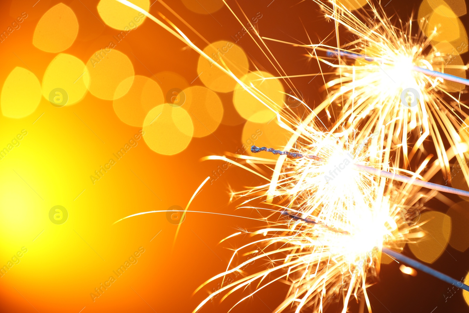 Photo of Bright burning sparklers on golden background with blurred lights, space for text. Bokeh effect