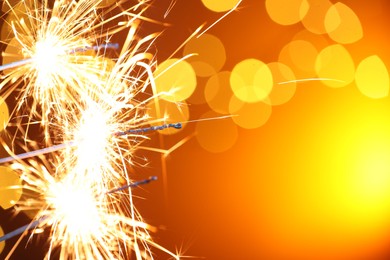 Photo of Bright burning sparklers on golden background with blurred lights, space for text. Bokeh effect