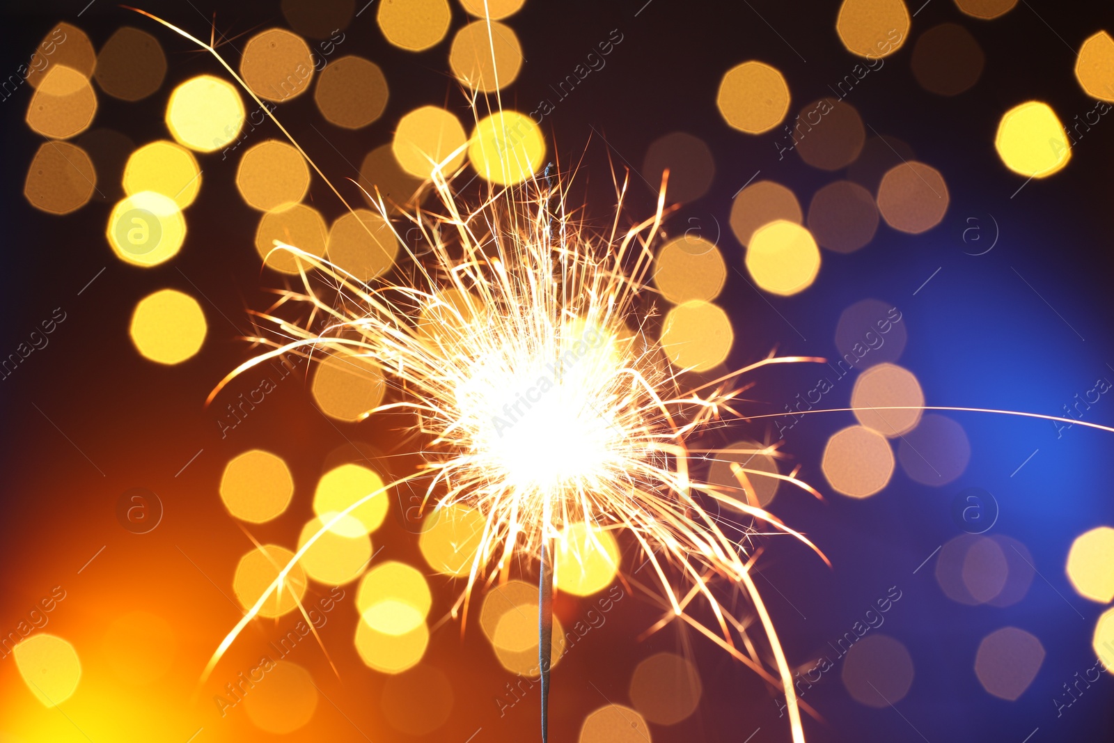 Photo of Bright burning sparkler on color background with blurred lights, bokeh effect