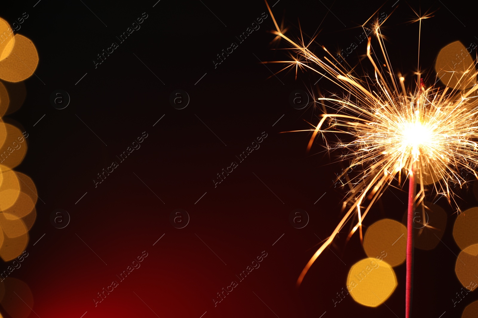 Photo of Bright burning sparkler on dark red background with blurred lights, space for text. Bokeh effect