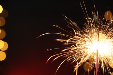 Photo of Bright burning sparkler on dark red background with blurred lights, space for text. Bokeh effect