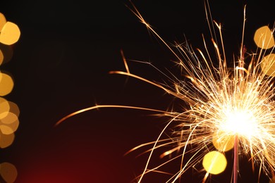 Photo of Bright burning sparkler on dark red background with blurred lights, space for text. Bokeh effect