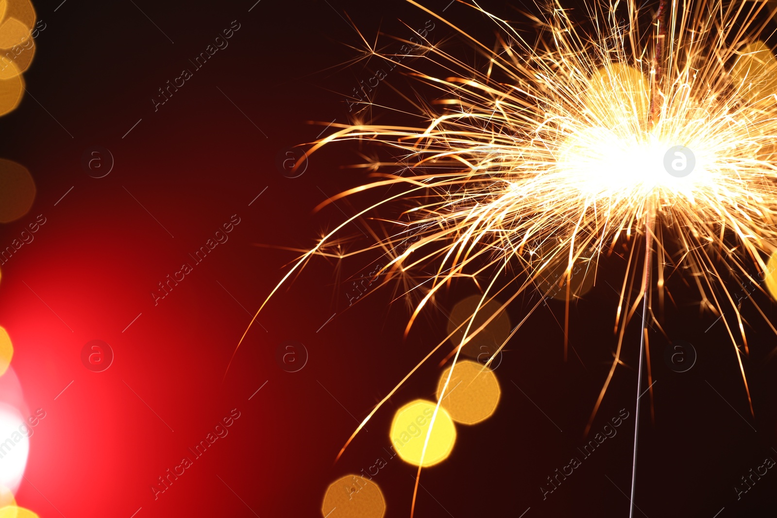 Photo of Bright burning sparkler on dark red background with blurred lights, space for text. Bokeh effect