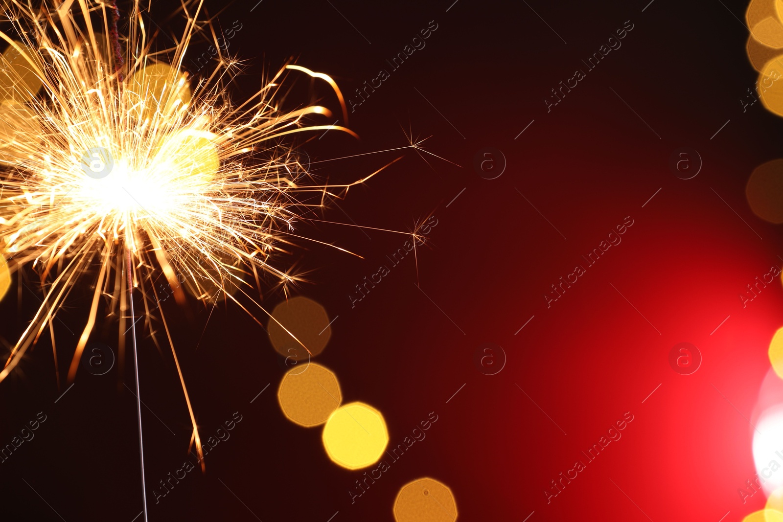 Photo of Bright burning sparkler on dark red background with blurred lights, space for text. Bokeh effect