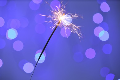 Photo of Bright burning sparkler on color background with blurred lights, bokeh effect