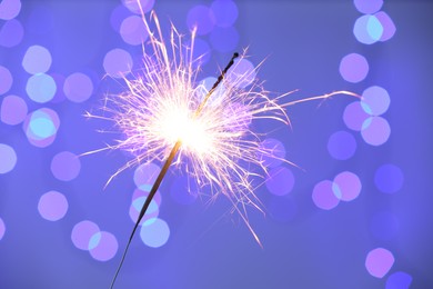 Photo of Bright burning sparkler on color background with blurred lights, bokeh effect