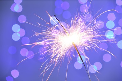 Photo of Bright burning sparkler on color background with blurred lights, bokeh effect