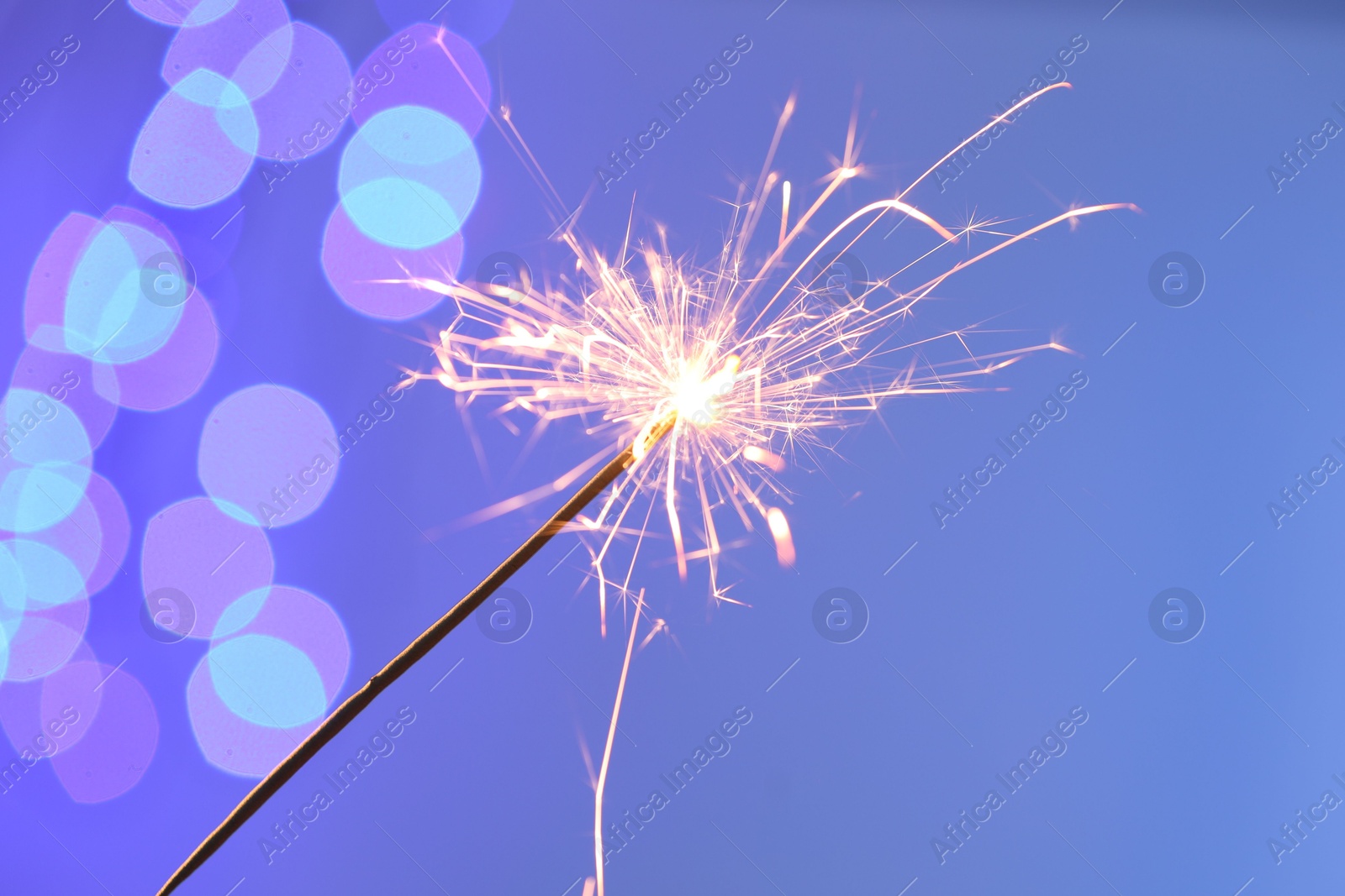 Photo of Bright burning sparkler on color background with blurred lights. Bokeh effect