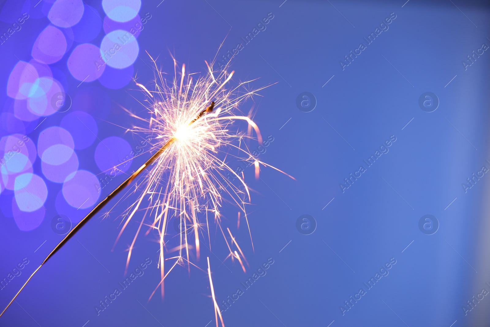 Photo of Bright burning sparkler on color background with blurred lights, space for text. Bokeh effect