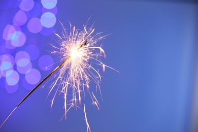 Photo of Bright burning sparkler on color background with blurred lights, space for text. Bokeh effect