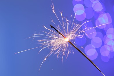 Photo of Bright burning sparkler on color background with blurred lights, bokeh effect