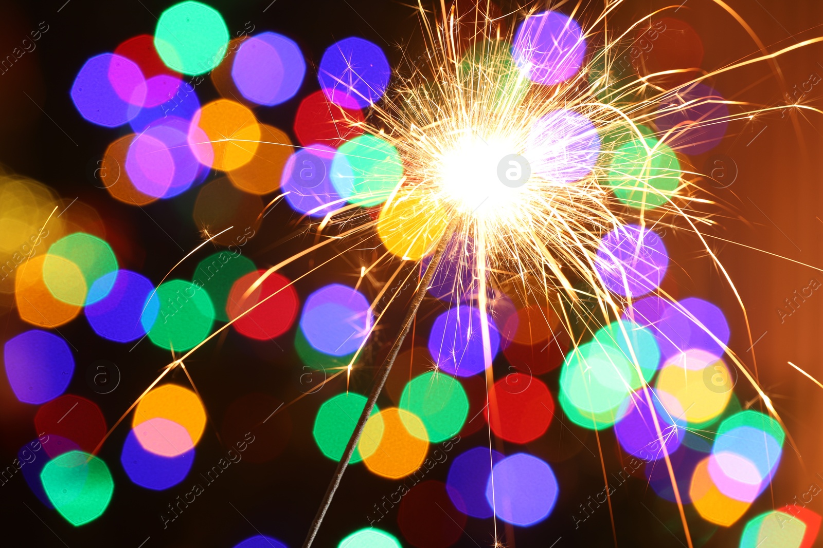 Photo of Bright burning sparkler on dark background with blurred lights, bokeh effect