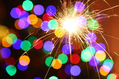 Photo of Bright burning sparkler on dark background with blurred lights, bokeh effect