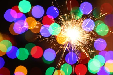 Photo of Bright burning sparkler on dark background with blurred lights, space for text. Bokeh effect